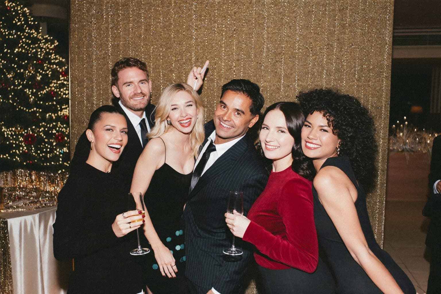 Coworkers laughing and posing with props in front of an open-air photo booth backdrop at a festive office holiday party