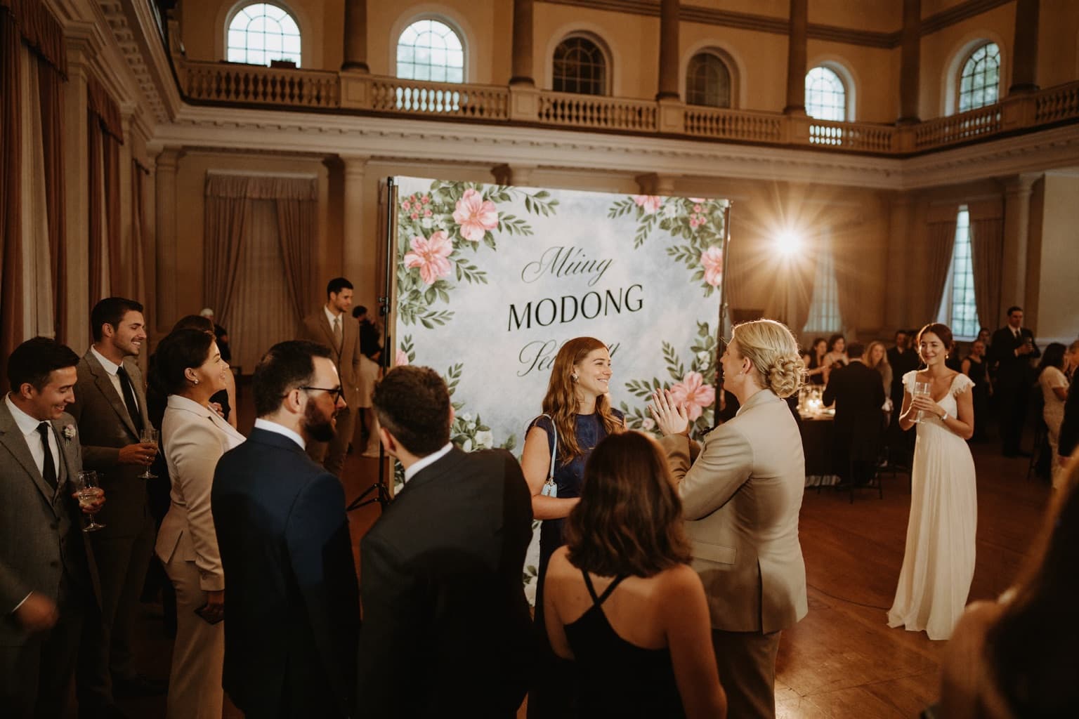 Guests posing at an open-air photo booth set up in a hotel ballroom during an evening reception.