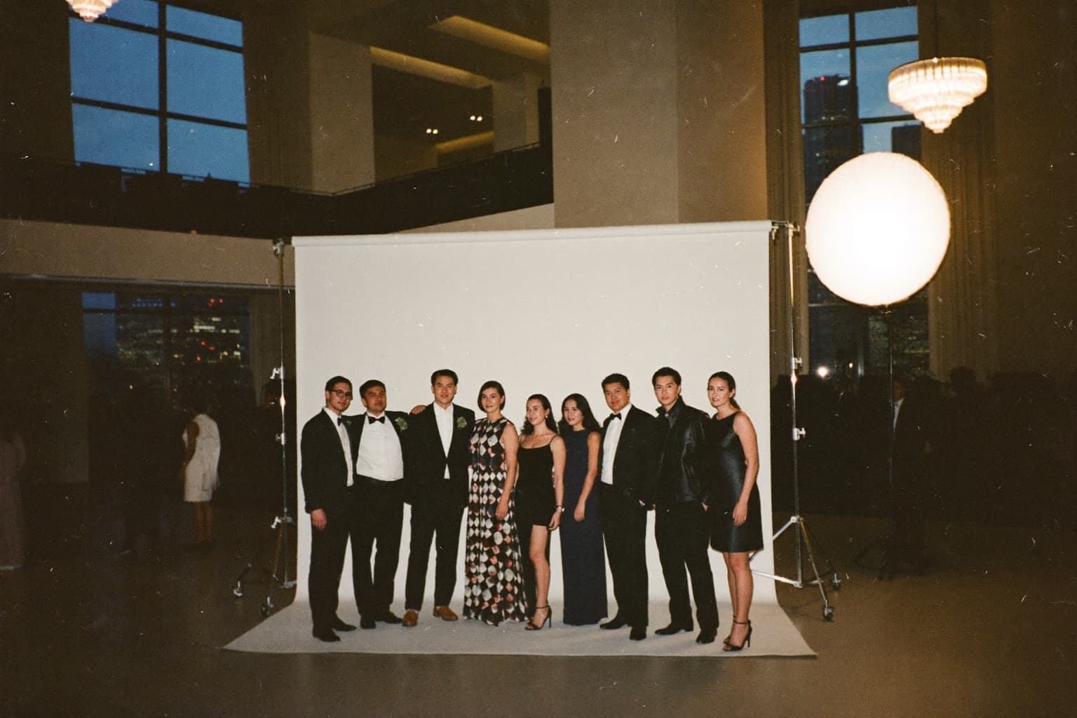Guests in formal wear holding photo strips beside a glam photo booth in a grand hotel ballroom during an evening gala.