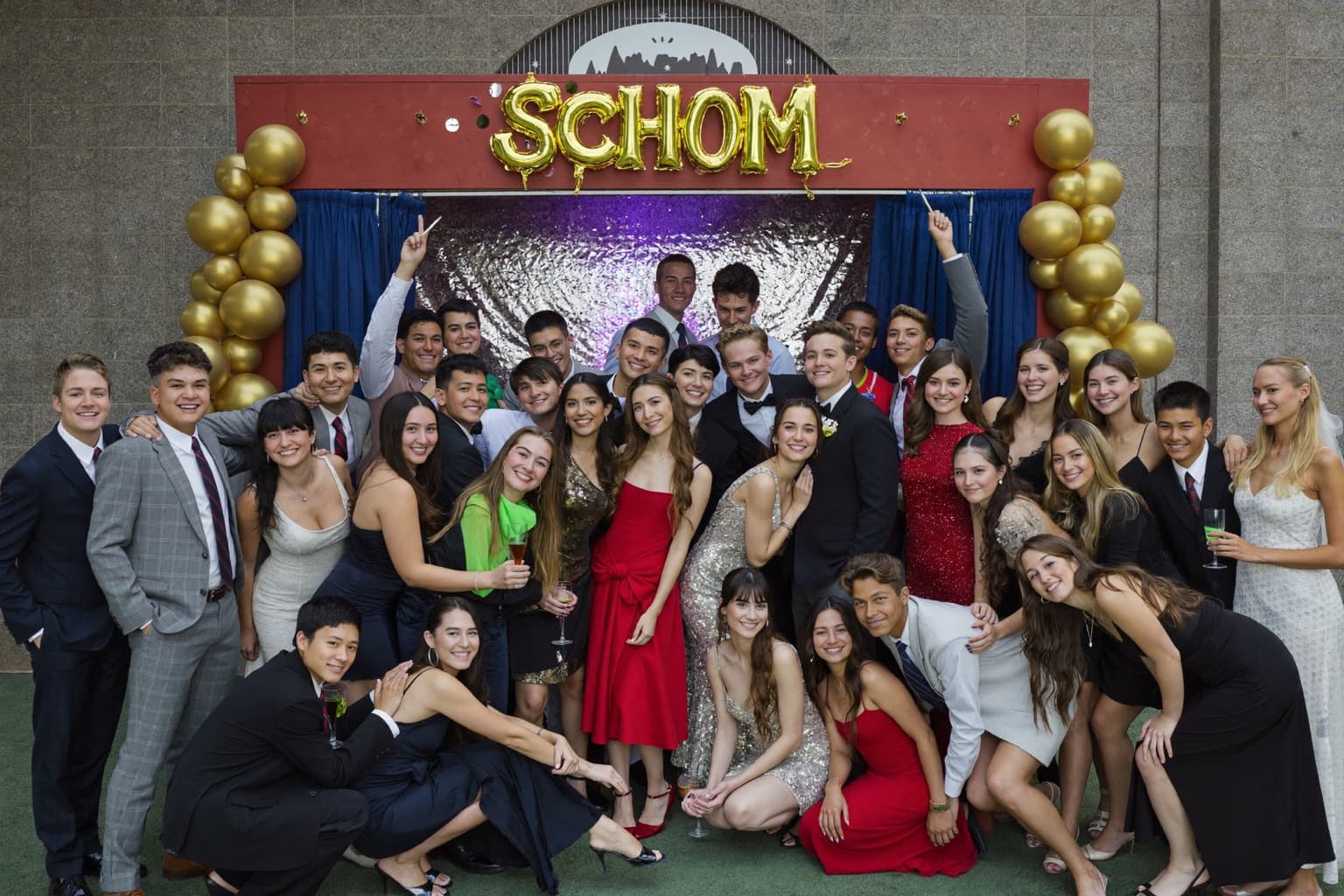 High school students in formalwear posing as a group at an open-air photo booth during a school dance