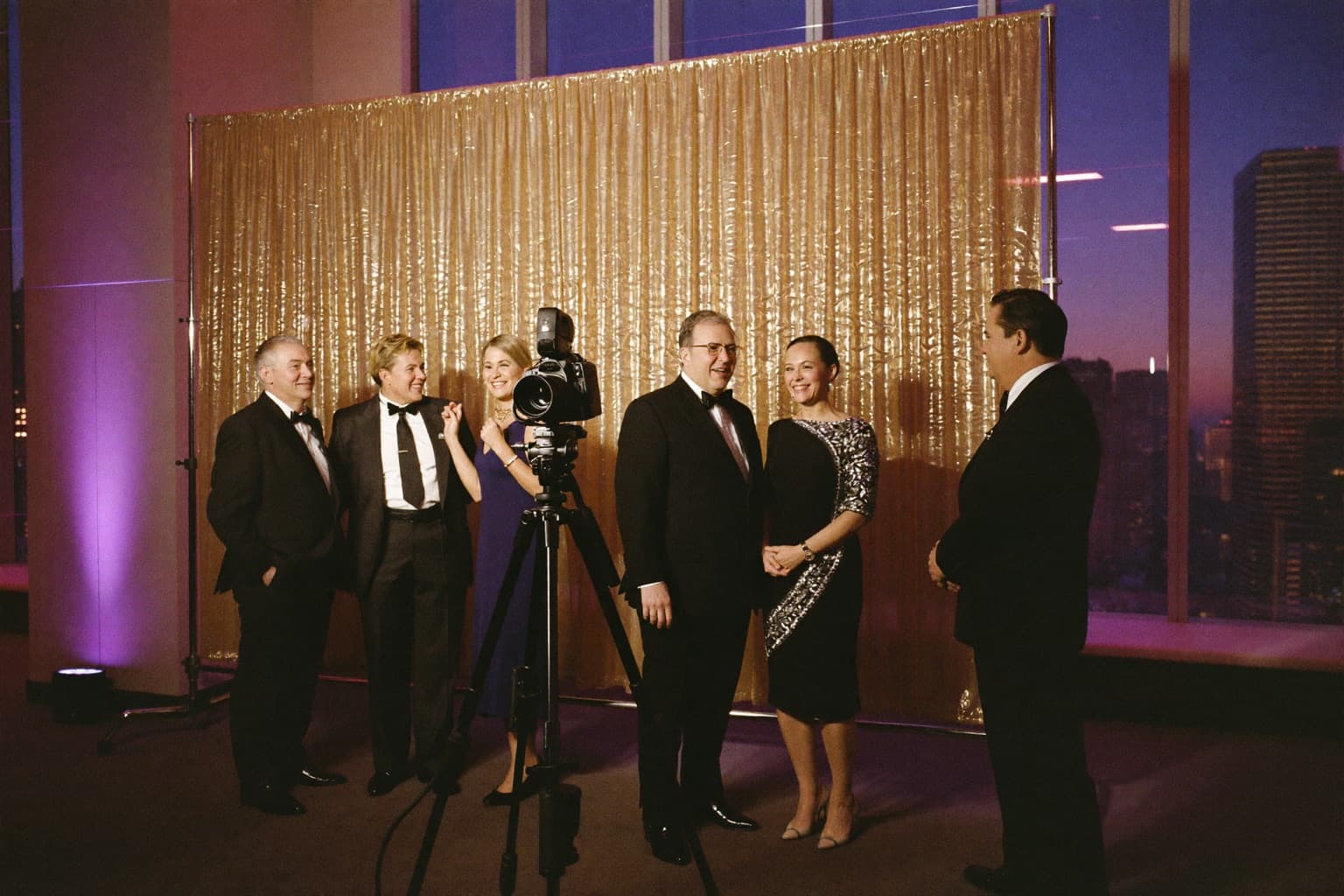 Professionals in cocktail attire posing with props at an open-air photo booth during a downtown corporate awards night.
