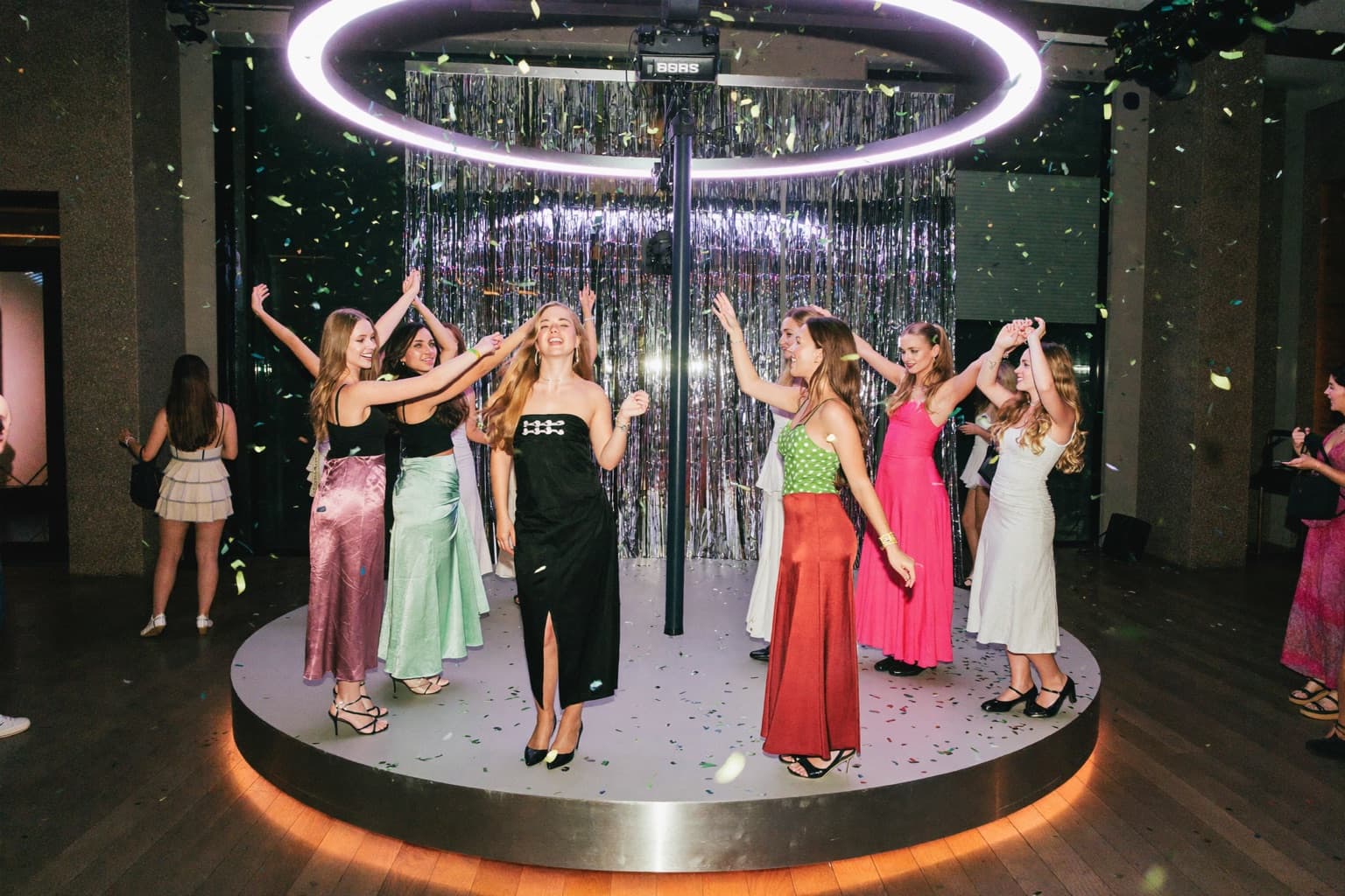 Teenage guests laughing on a 360 photo booth platform as the camera arm spins around them at a party with string lights